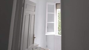 Un couloir avec un ventilateur de plafond, une porte donnant sur une pièce et une fenêtre offrant une vue sur la verdure à l’extérieur.