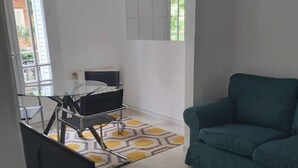 Un salon avec un canapé vert, un fauteuil noir, une petite table et un téléviseur posé sur un meuble.