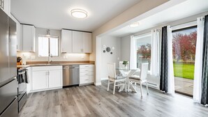 Une cuisine moderne avec des meubles blancs, un four encastré et un coin repas comprenant une table et des chaises en verre.