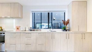 A modern kitchen with light wood cabinets, a large window, and a view of the city.