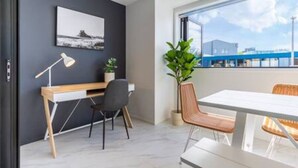 A modern room with a desk, chair, and dining table. There is a window with a view of buildings and a plant on the windowsill.