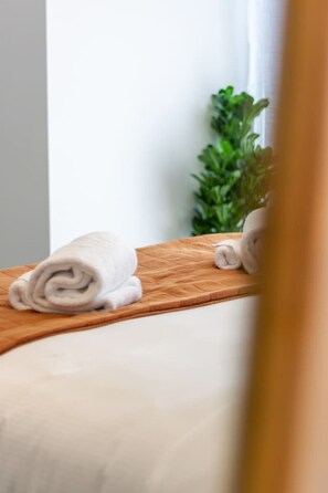 Cama bien tendida con sábana blanca y toalla enrollada de color blanco sobre cabecera de madera.