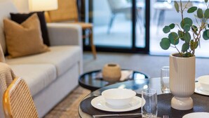 A modern living room with a sofa, a coffee table, and a dining table set with plates and glasses. - Modern CBD Central Stay - Hagley Park + Balcony (Christchurch)