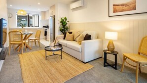A modern living room with a sofa, coffee table, and chairs. A kitchen is visible in the background. - Modern CBD Central Stay - Hagley Park + Balcony (Christchurch)