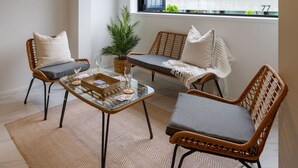 A cozy seating area with wicker chairs and a glass table, a potted plant, and a view of buildings through a window. - Modern CBD Central Stay - Hagley Park + Balcony (Christchurch)