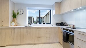 A modern kitchen with light wood cabinets, a large window, and a stainless steel oven. - Modern CBD Central Stay - Hagley Park + Balcony (Christchurch)