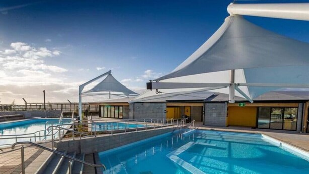 A swimming pool area with clear blue water, steps leading into the pool, and a covered seating area with a view of the pool. - Okioki - Seaside Escape (Christchurch)