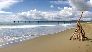 A beach with a wooden structure and a pier in the background. - Okioki - Seaside Escape (Christchurch)