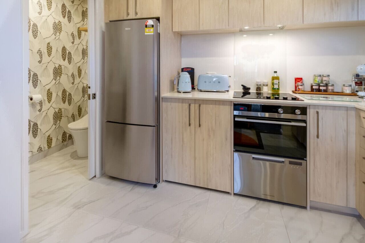 Cozinha moderna com eletrodomésticos de aço inoxidável, armários de madeira clara e painel de azulejos.