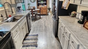 A kitchen with wooden cabinets, a refrigerator, a dining table with chairs, and a rug. - Creekside Cottage Near Nashville- Pet Friendly! (Pegram)