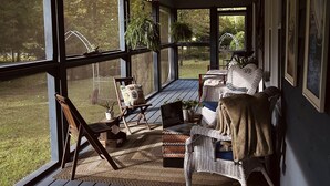 A covered porch with wicker furniture, a laptop, and a lantern. - Creekside Cottage Near Nashville- Pet Friendly! (Pegram)