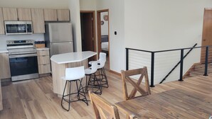 Une cuisine moderne dotée d’appareils électroménagers en acier inoxydable, un coin repas avec une table blanche et des tabourets de bar, et un plancher en bois.