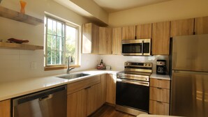 Une cuisine moderne dotée de meubles en bois, d’appareils électroménagers en acier inoxydable, d’un lave-vaisselle et d’une fenêtre qui laisse entrer la lumière naturelle.