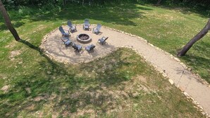 Un espace extérieur aménagé avec des chaises Adirondack disposées autour d’un foyer central, le tout bordé de pierres.