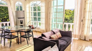 A spacious living area with a glass table, black chairs, a dark sofa, and a balcony with a view of greenery. - 9 Bed 6bath  Pool, Roof lounge, Beach Best location in Playa Walk to everything (Playa del Carmen)