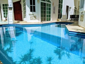 A clear blue swimming pool with a tiled edge, a wooden door, and a window with a white frame.