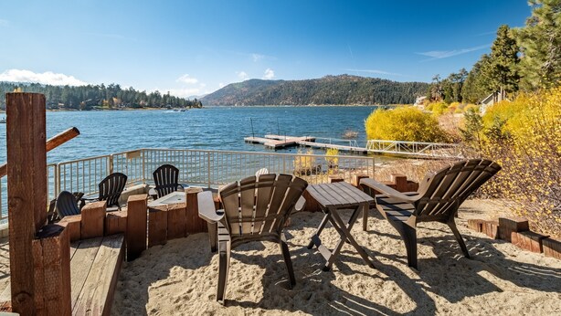 Eine Holzterrasse mit Stühlen und Tischen mit Blick auf einen See, einen Steg und einen bewaldeten Hügel.