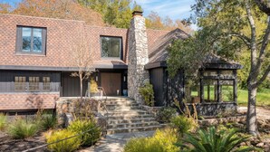 A modern house with a stone chimney, a wooden deck, and a stone staircase leading to the entrance. - Malvasia by Avantstay Luxe Wine Country Retreat (Santa Rosa)