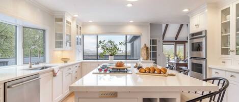 A modern kitchen with white cabinetry, a central island, and a large window providing natural light.