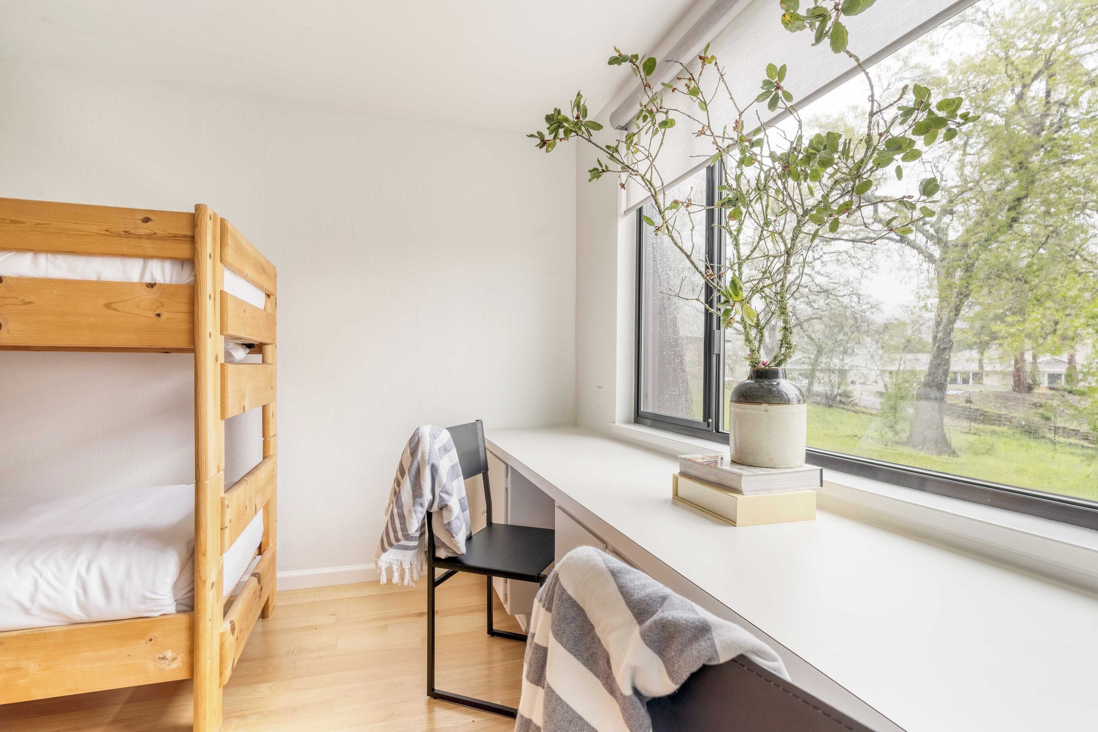 A bunk bed with a window view, a desk with a chair, and a potted plant.