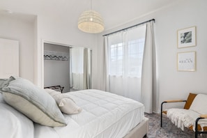 Ein Schlafzimmer mit Bett, Sessel, Kleiderschrank und einem Fenster mit Vorhängen.
