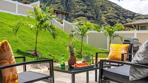 Une terrasse avec des meubles d’extérieur, un barbecue et une vue sur une colline verdoyante.