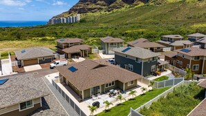 Un quartier résidentiel avec des maisons modernes, un espace de stationnement et une vue sur l’océan, avec une montagne en arrière-plan.