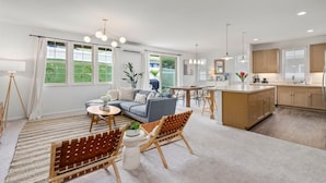 Un salon moderne comprenant un canapé, des fauteuils, un coin repas et une cuisine avec des meubles en bois et une grande fenêtre.