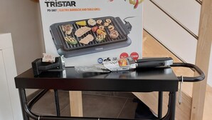 A black metal cart with a box of a Tristar electric barbecue and table grill, a power strip, and a small grill on top. - Maison Neuve Bord de mer (Lion-sur-Mer)