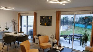 A modern living room with a dining area, large windows, and a view of the outdoors. - Maison Neuve Bord de mer (Lion-sur-Mer)