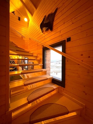 A wooden interior with a staircase, a large window, and a mounted animal head.