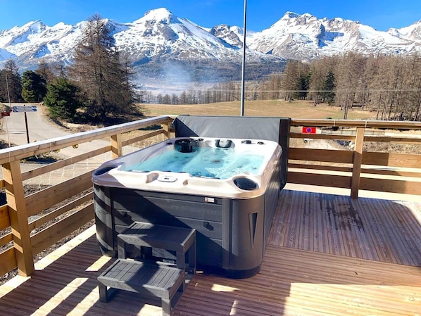 A hot tub on a wooden deck with a mountain view.