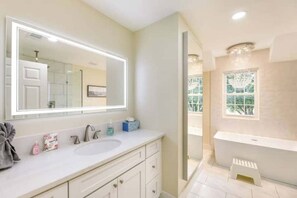 A bathroom with a large mirror, a sink, a bathtub, and a window.