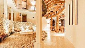 Un vaste espace intérieur agrémenté d’un mur en pierre, d’une fontaine et d’un escalier en bois.