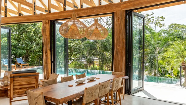 Un vaste espace dédié à la salle à manger, avec une grande table et des chaises en bois, de grandes fenêtres offrant une vue sur une piscine et une végétation luxuriante.
