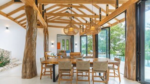 Un espace repas avec une table et des chaises en bois, de grandes fenêtres et une vue sur la verdure.
