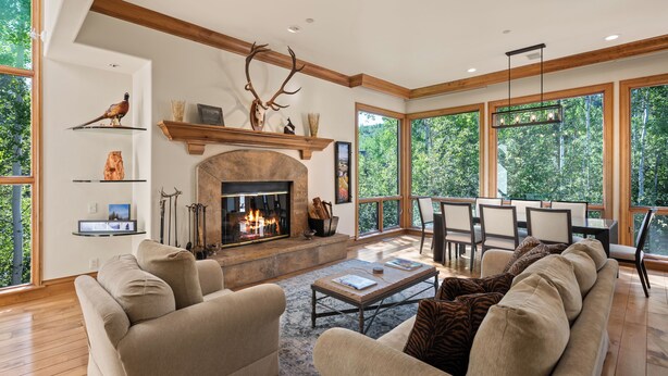 A spacious living room with a fireplace, comfortable seating, and large windows offering a view of the outdoors. - Two Creeks by Snowmass Vacations (Snowmass Village)