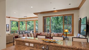 A kitchen with granite countertops, a double sink, and large windows offering a view of trees. - Two Creeks by Snowmass Vacations (Snowmass Village)