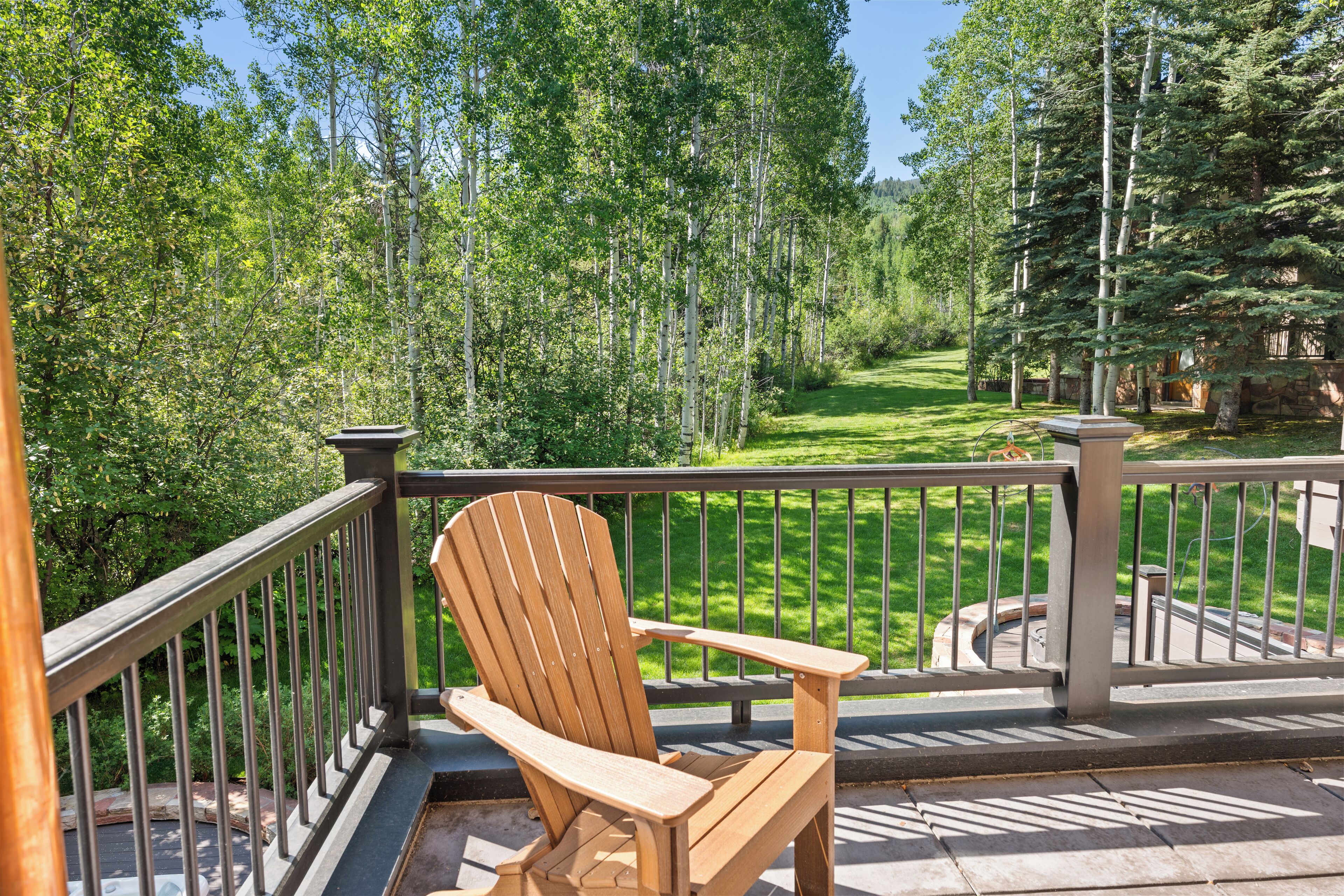 A wooden Adirondack chair on a balcony with a view of a well-maintained lawn and trees.