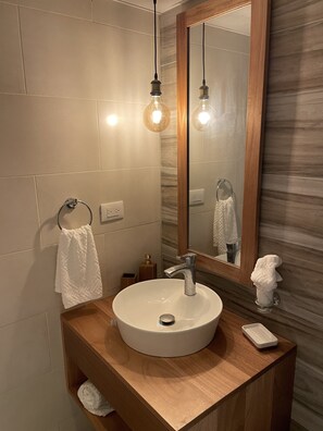 Ein modernes Badezimmer mit einem runden Waschbecken, einem Holzwaschtisch und einem großen Spiegel.