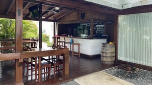 Eine hölzerne Außenbereich-Sitzgelegenheit mit Tischen und Stühlen, eine Bar mit Theke und ein großes Fass.