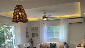 Ein Essbereich mit einem weißen Tisch, gedeckt für vier Personen, einem Deckenventilator und Blick ins Freie durch große Fenster.
