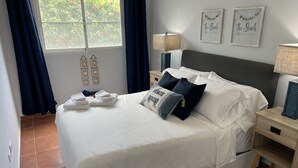 Ein ordentlich bezogenes Bett mit weißen Leinentüchern, ein Kissen mit der Aufschrift 'The Beach House' und zwei sternförmige Wanddekorationen.