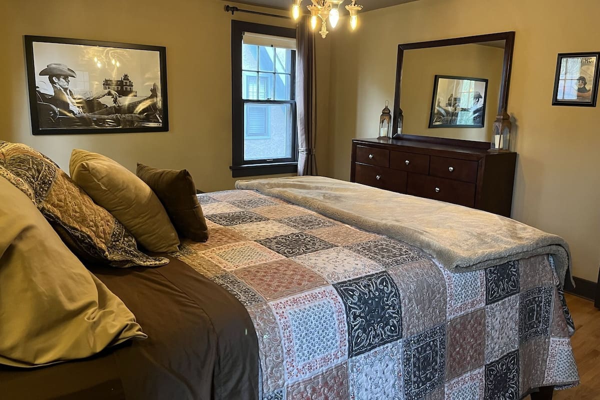 A bedroom with a bed, a dresser, a chandelier, and two framed pictures on the wall.