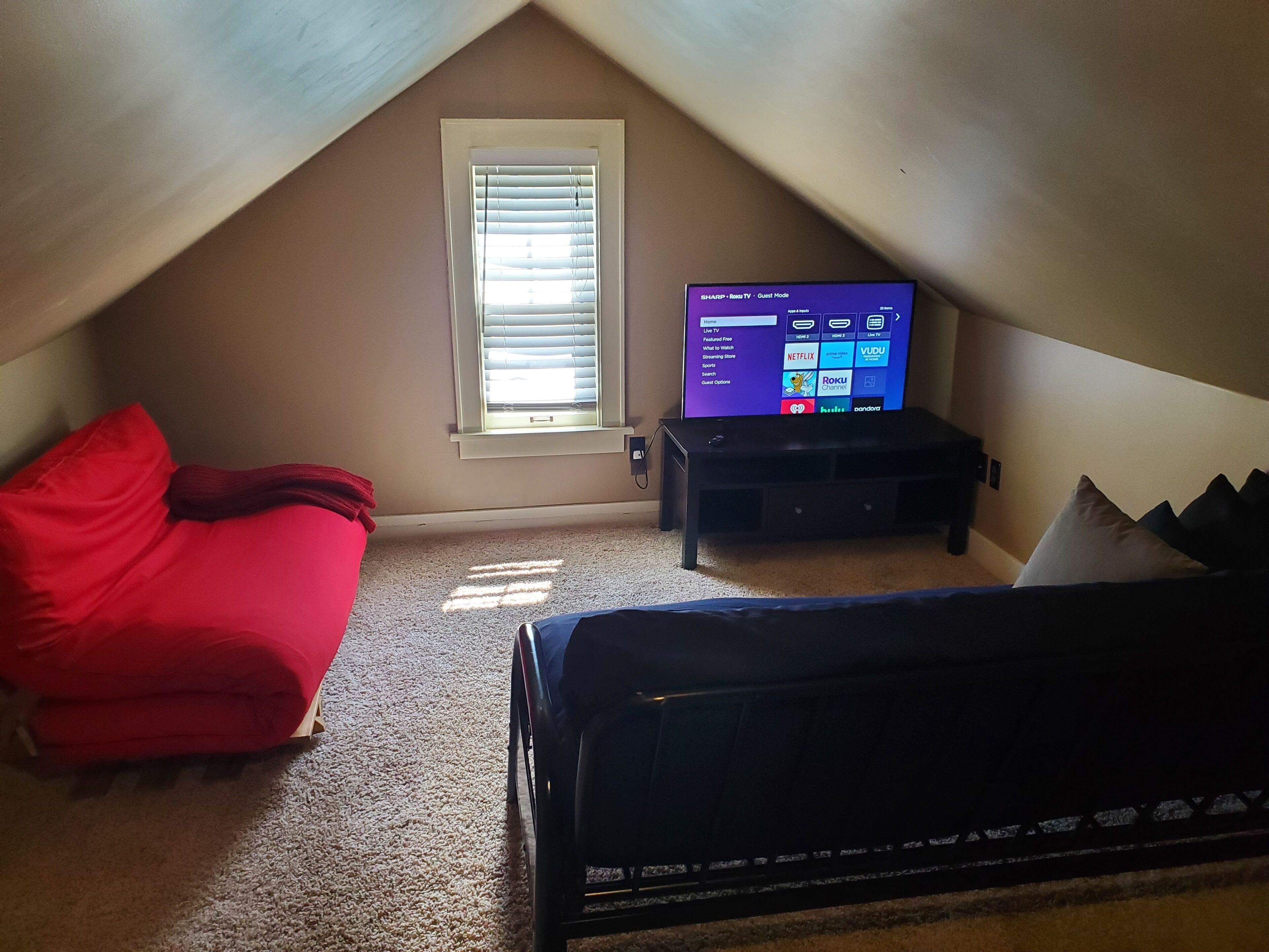 A small, sloped room with a TV on a stand, a red couch, and a bed.