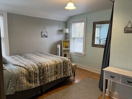 A bedroom with a bed, bedside lamp, radiator, and a small shelf with decorative items.
