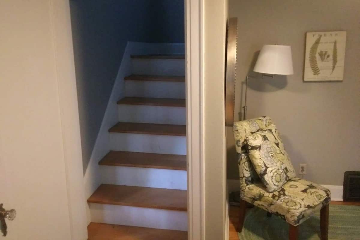 A staircase leading to a second floor, a patterned armchair, a floor lamp, and a framed botanical print on the wall.