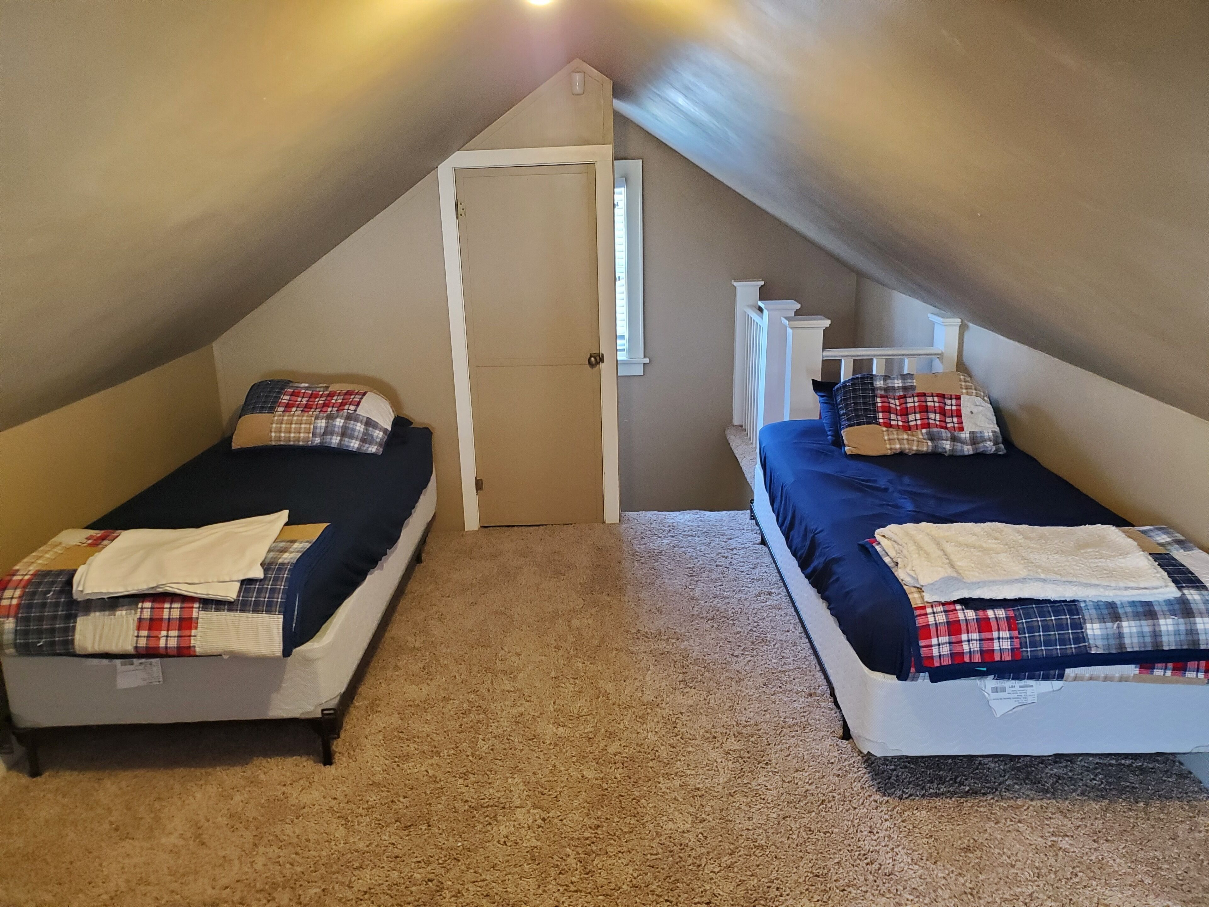 A small attic bedroom with two single beds, each with a plaid blanket and pillow.