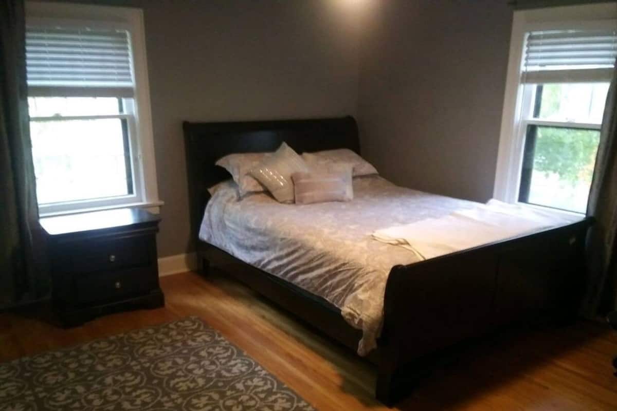 A bedroom with a bed, two nightstands, a patterned rug, and a window with blinds.