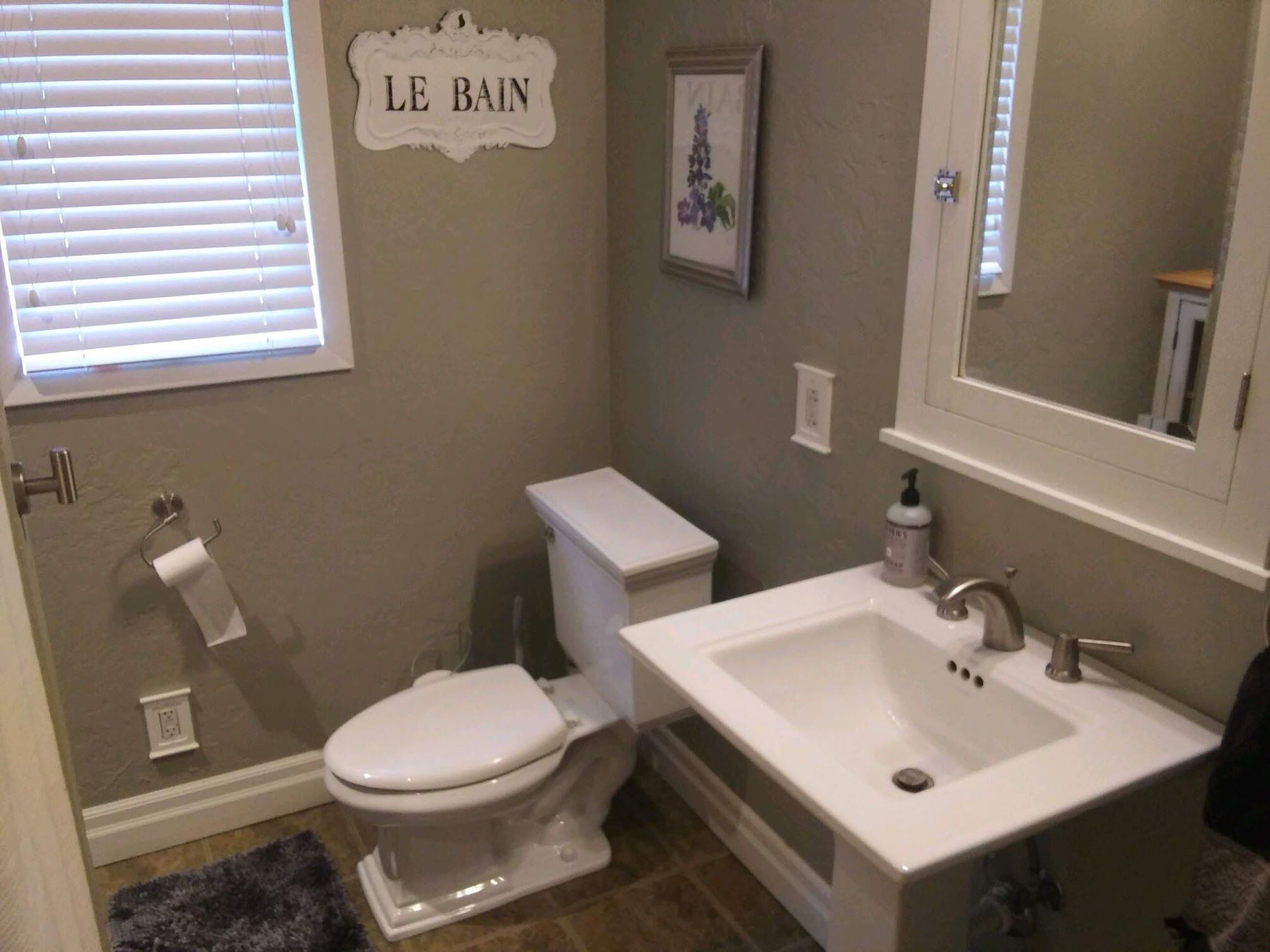 A bathroom with a toilet, sink, and a window with blinds.
